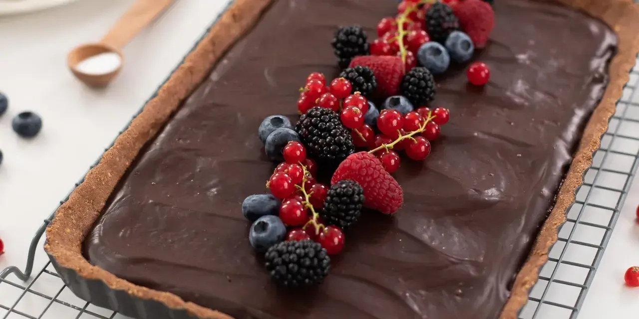 Tarta de chocolate cremosa decorada con frutos rojos frescos: frambuesas, moras, arándanos y grosellas.