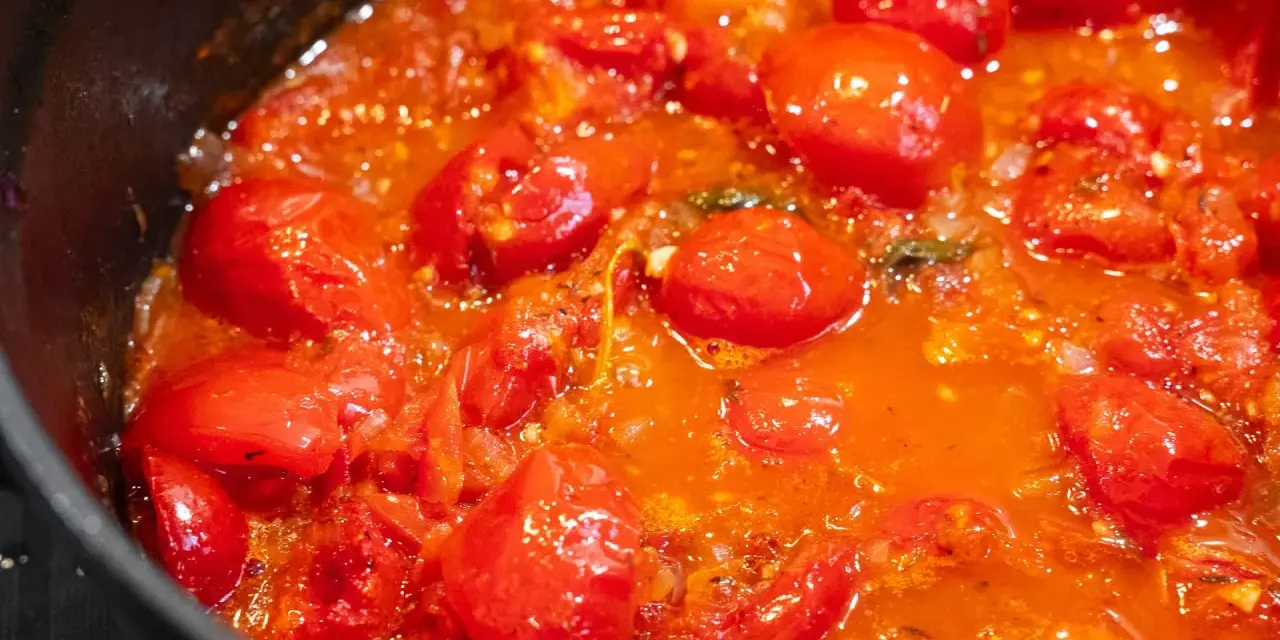 Ein köstliches, blubberndes Tomaten Sugo in einer schwarzen Pfanne, voller saftiger Kirschtomaten und aromatischer Kräuter.