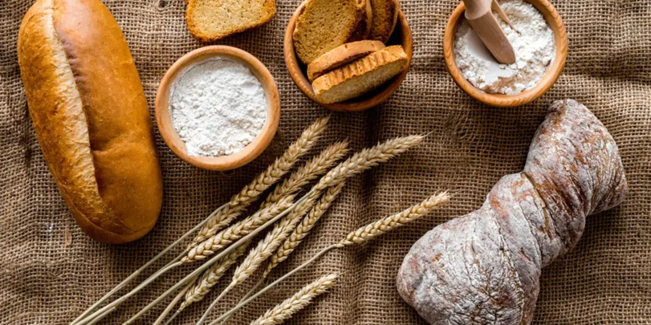 Brot, Getreideähren und Schalen mit Mehl, darunter Vollkornmehl aus Deutschland, liegen auf Jute.