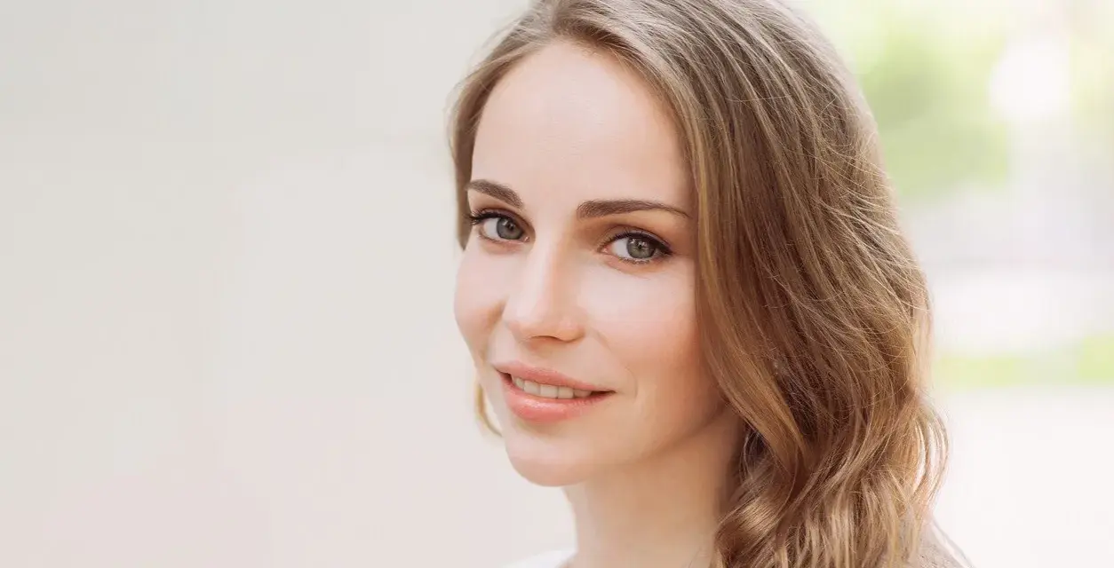 Uśmiechnięta kobieta z mysi blond włosami, delikatnie falującymi na ramionach.