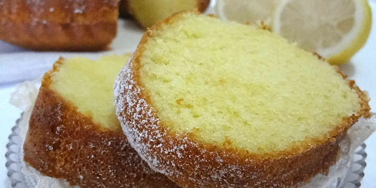 Fette di ciambellone al limone spolverate di zucchero a velo, con fette di limone sullo sfondo.