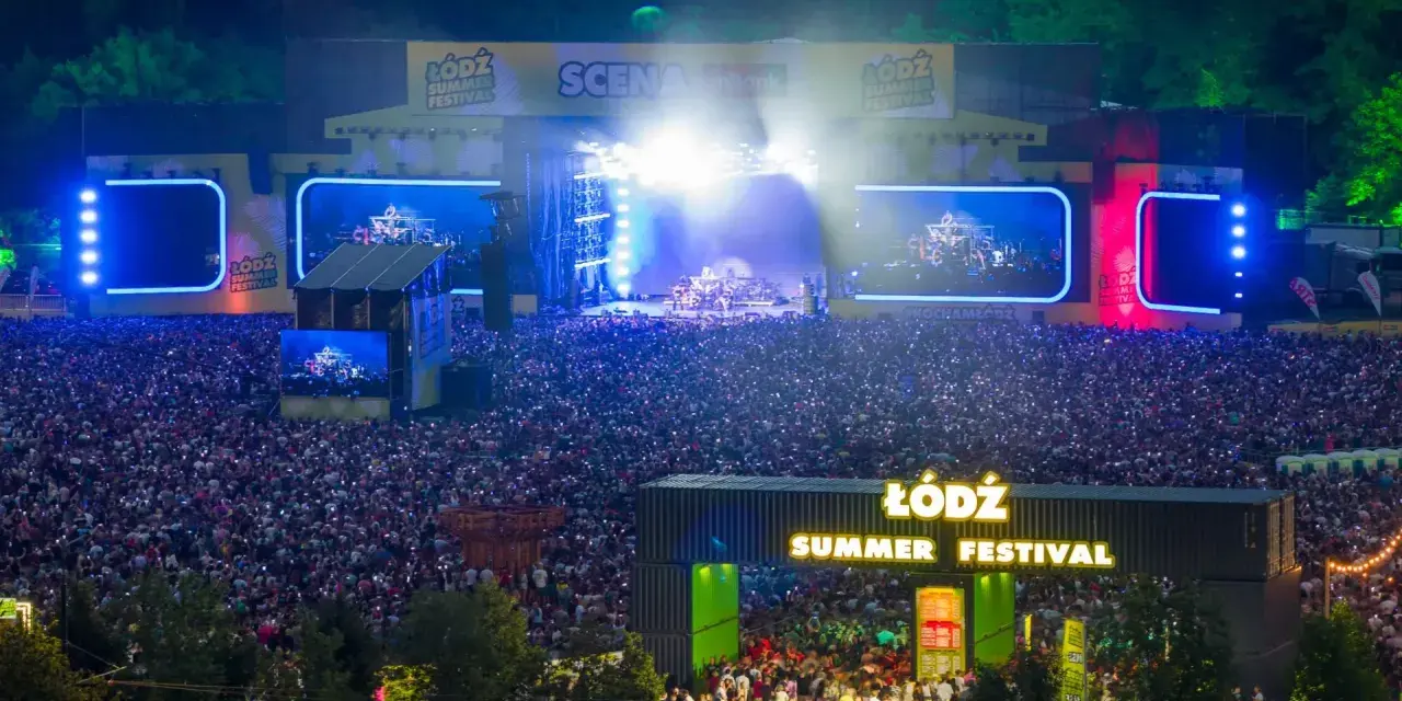 Tłum ludzi na koncercie podczas Łódź Summer Festival 2026. Na scenie gra zespół, a widzowie oświetlają teren telefonami.