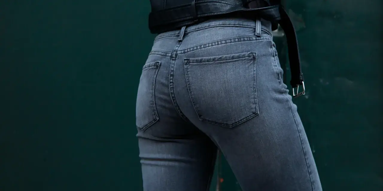 Vue arrière d'une femme portant un jean gris à coupe ajustée, avec une veste en cuir noir.