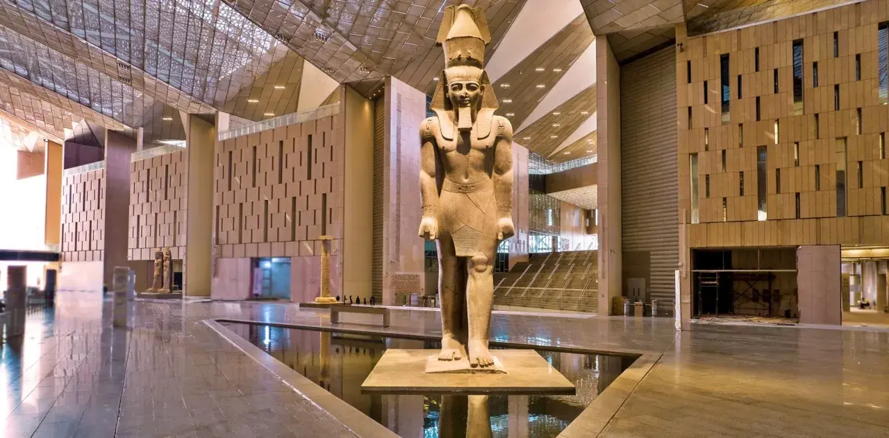 Gigantyczny posąg faraona w holu nowego muzeum w Egipcie, z nowoczesną architekturą i wodnymi elementami.