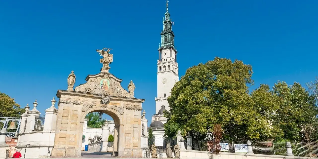 Brama na Jasną Górę, gdzie pielgrzymi zastanawiają się, ile ma lat to miejsce o bogatej historii. Wieża klasztoru góruje nad zielenią.