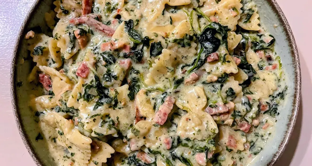 Pyszny makaron farfalle ze szpinakiem i kawałkami boczku w kremowym sosie.