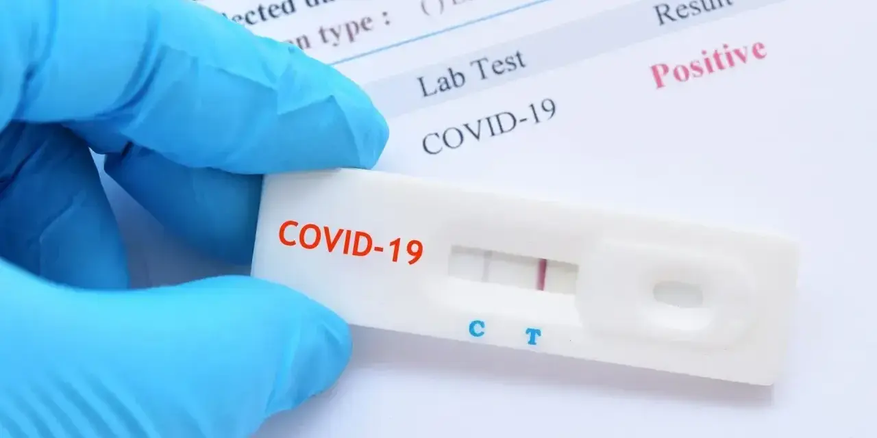 Rękawiczka ochronna trzyma test antygenowy COVID-19 z pozytywnym wynikiem.