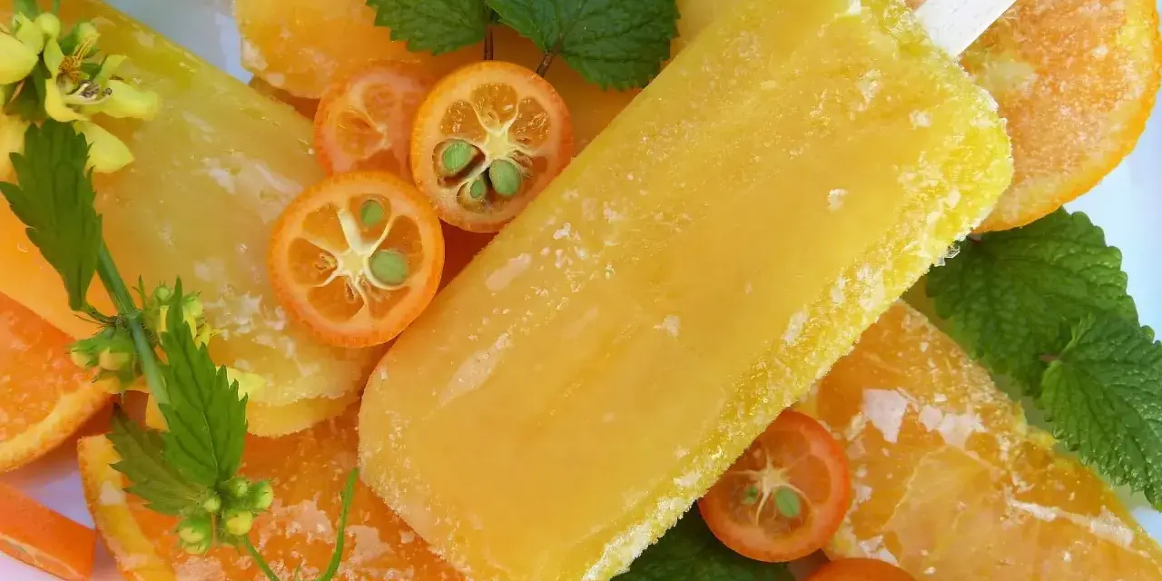 Paletas de helado de naranja, rodajas de naranja y kumquats adornan esta refrescante escena veraniega.