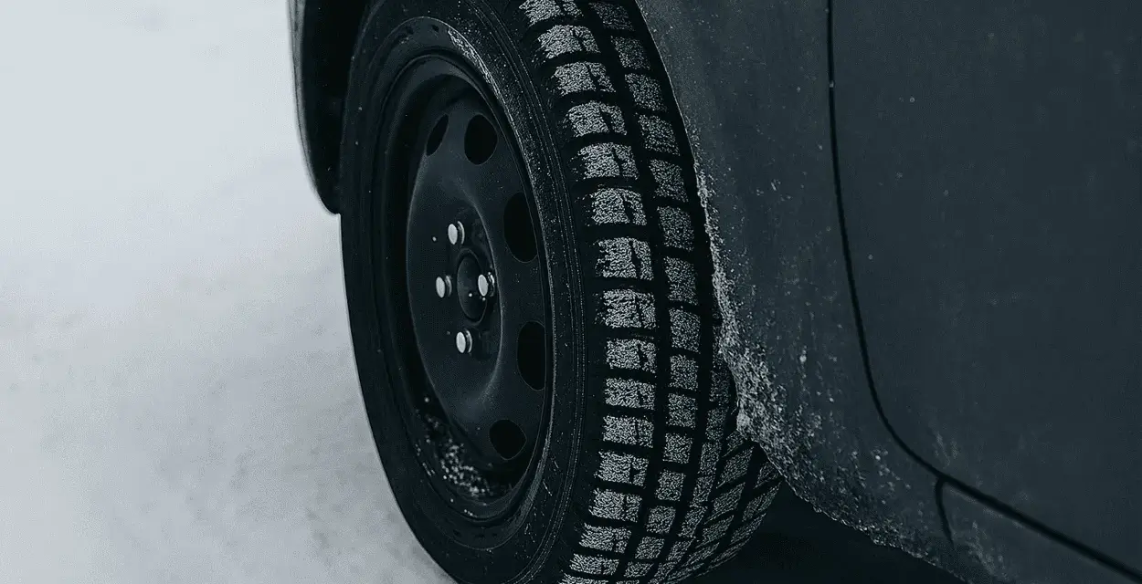 Ruota di un'auto con pneumatico invernale coperto di brina, pronto per affrontare la neve. La scheda pneumatici è fondamentale per la sicurezza.