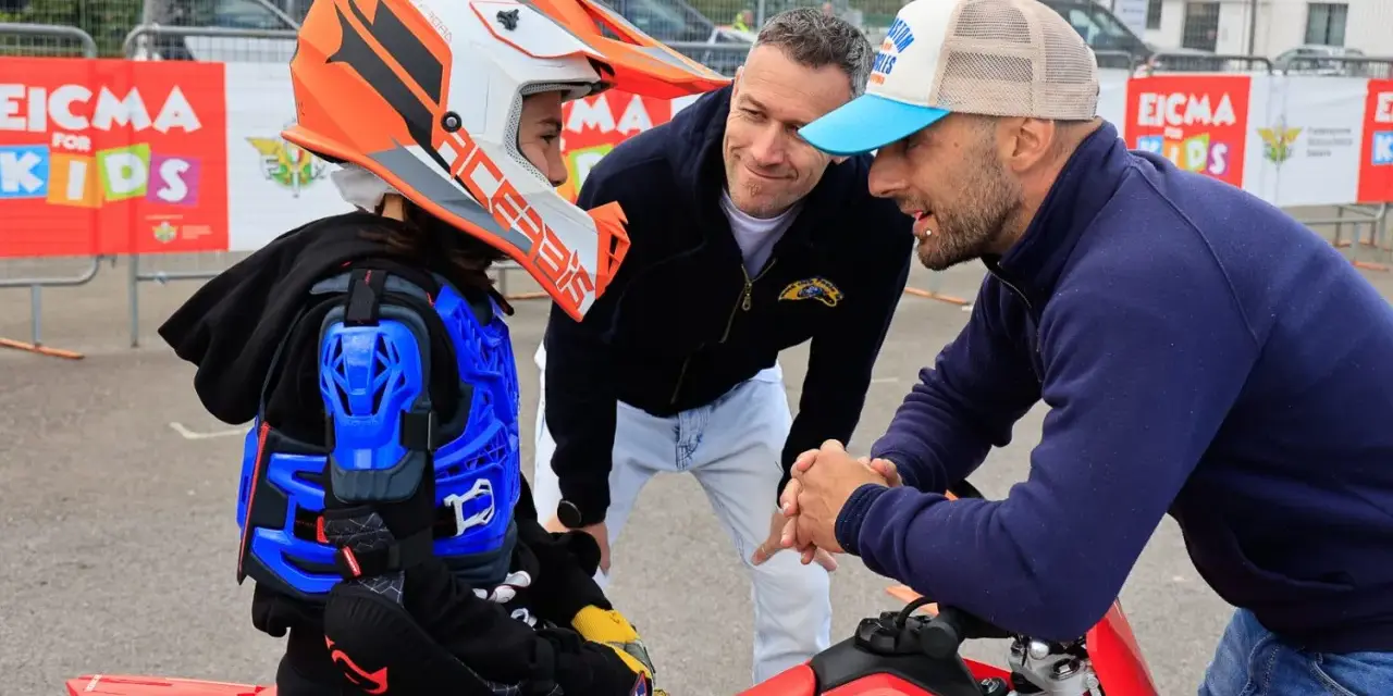 Giovane motociclista donna con casco e protezioni, ascolta i consigli di due uomini.
