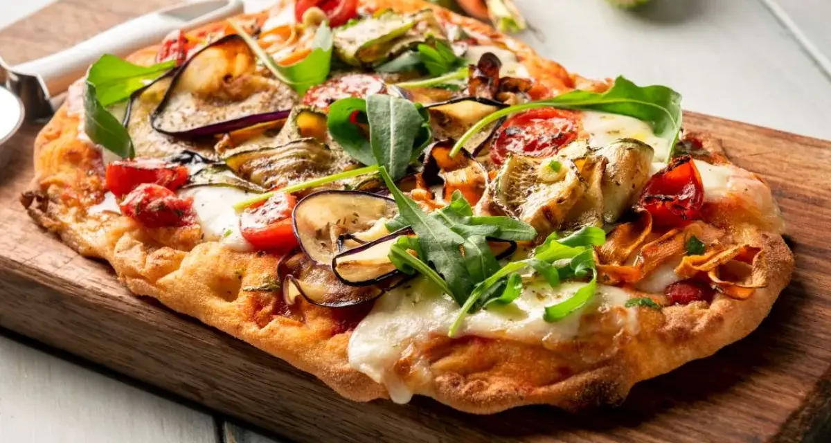Chrupiący spód do pizzy z bakłażanem, cukinią i pomidorkami, posypany rukolą i mozzarellą.