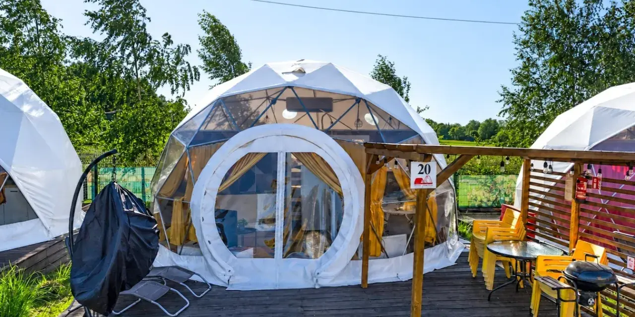Nowoczesne namioty sferyczne na energylandia pole namiotowe. Drewniany taras z grillem i żółtymi krzesłami.