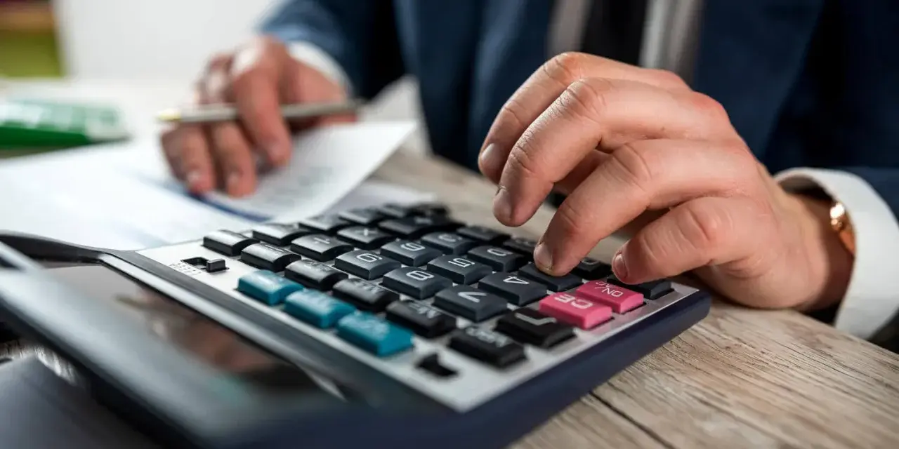 Man con traje calculando en calculadora. Los suplidos llevan IVA, un detalle importante en la contabilidad.