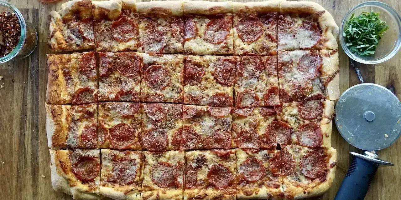 Domowa pizza na blachę z pepperoni, posypana parmezanem. Idealna na rodzinne spotkanie.