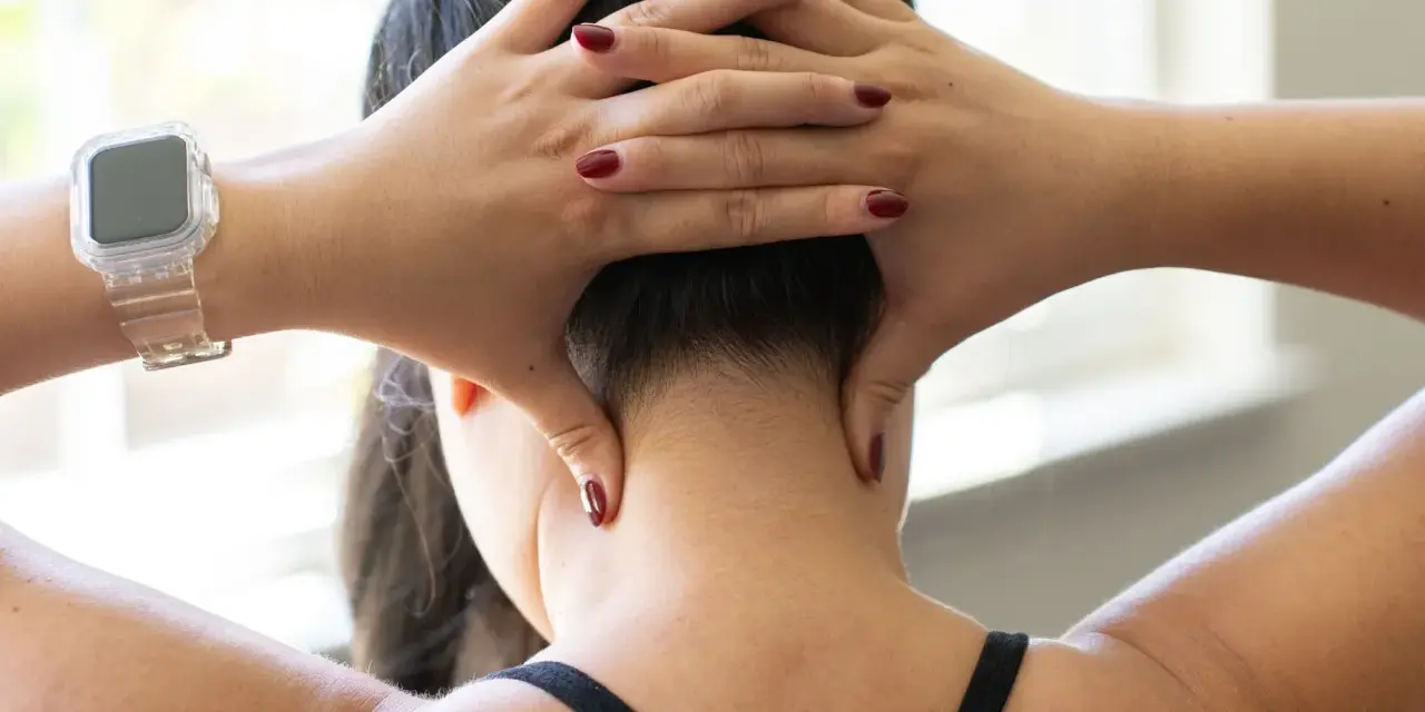 Hands demonstrate shiatsu self neck massage techniques, applying pressure to the base of the skull and sides of the neck.