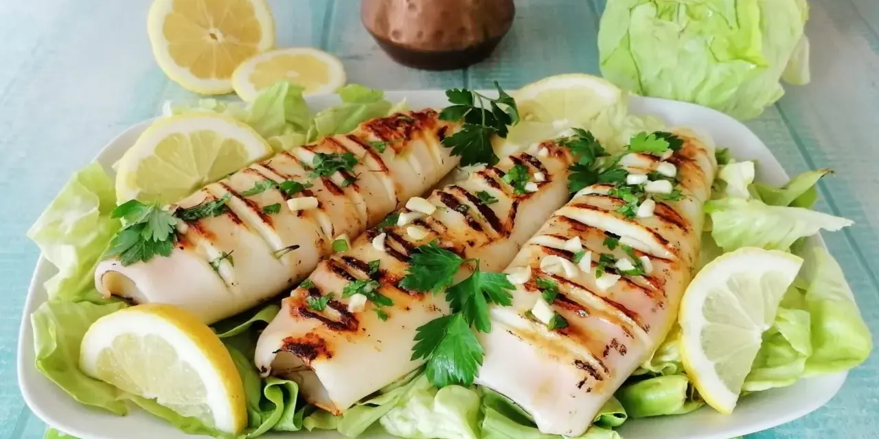 Tre calamari alla griglia, conditi con aglio e prezzemolo, serviti su un letto di lattuga con spicchi di limone.