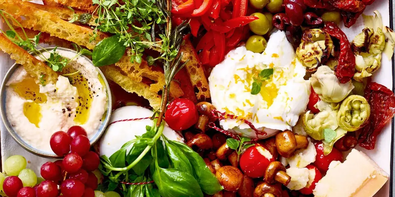 Eine Platte mit geilen Snacks: Hummus, Burrata, Trauben, Brot, Oliven, Pilze, Tomaten und Käse.