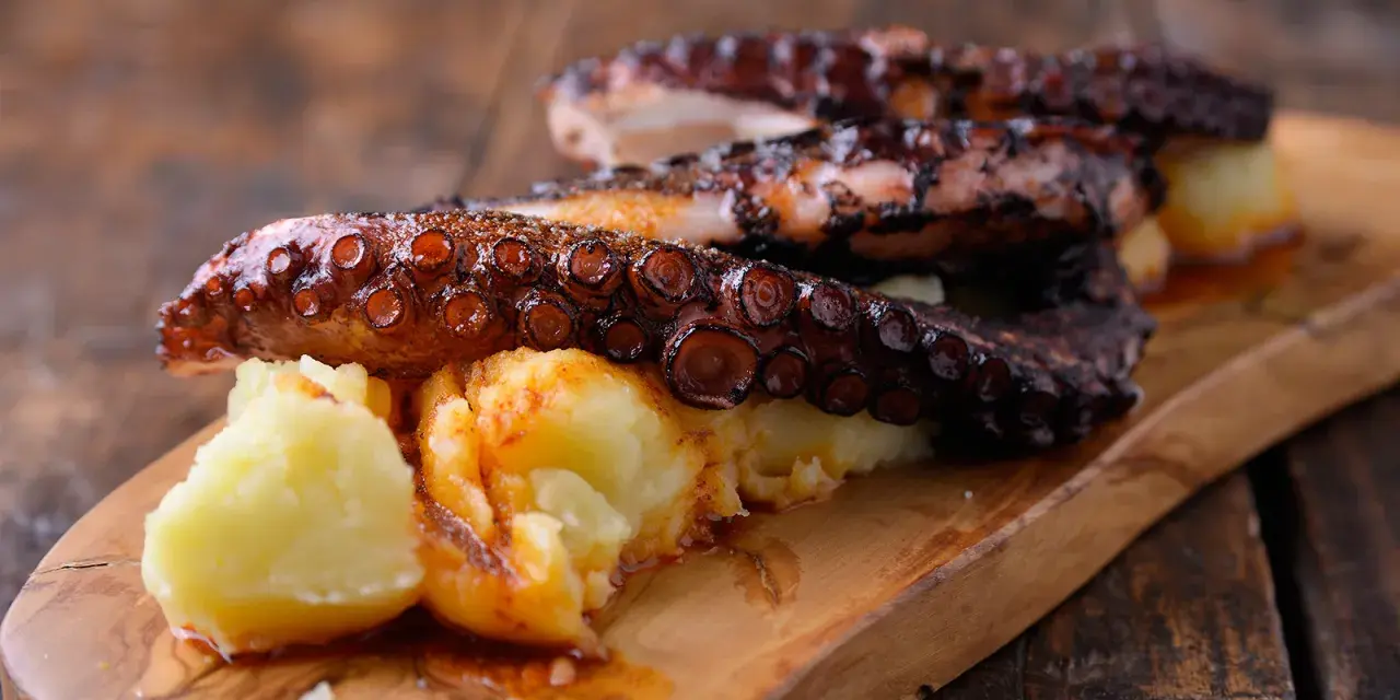 Pulpo tierno con patatas cocidas y espolvoreado con pimentón, servido en tabla de madera.