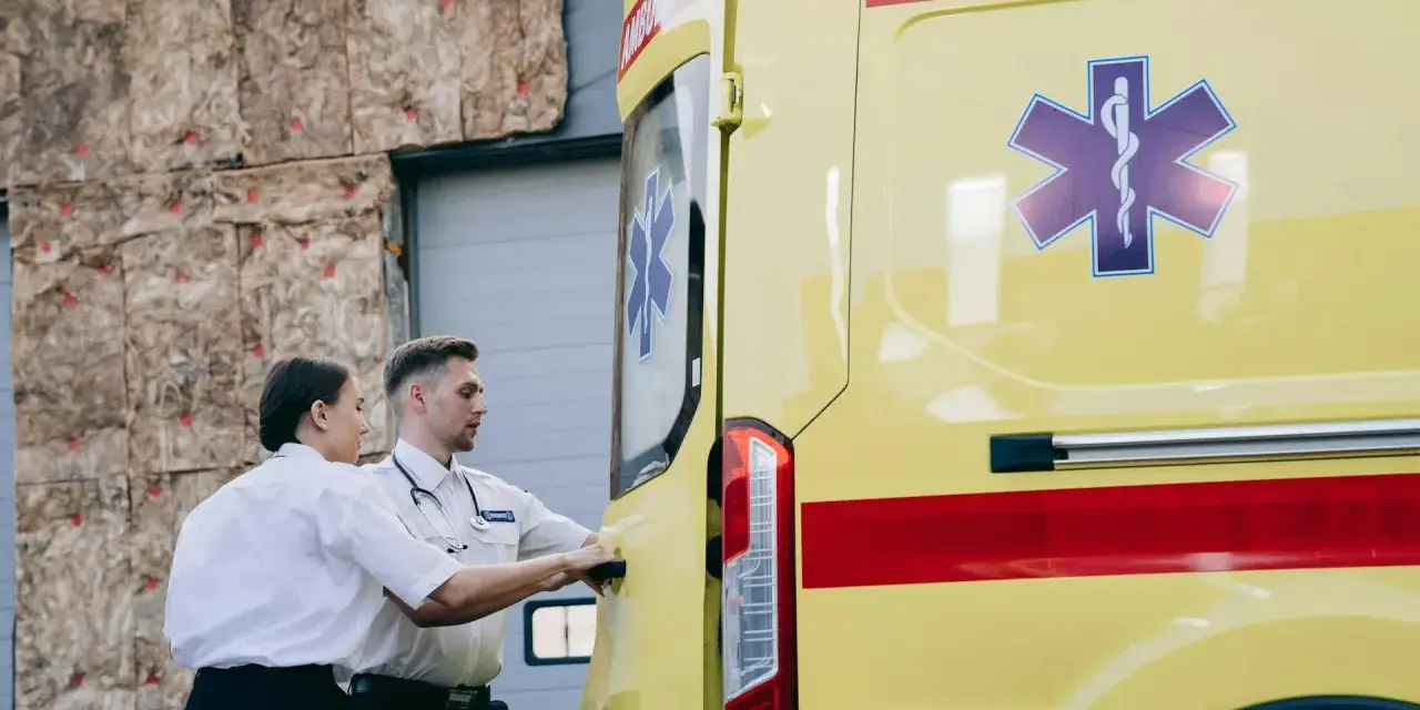 Ratownicy medyczni przy żółtej karetce z symbolem Gwiezdy Życia.