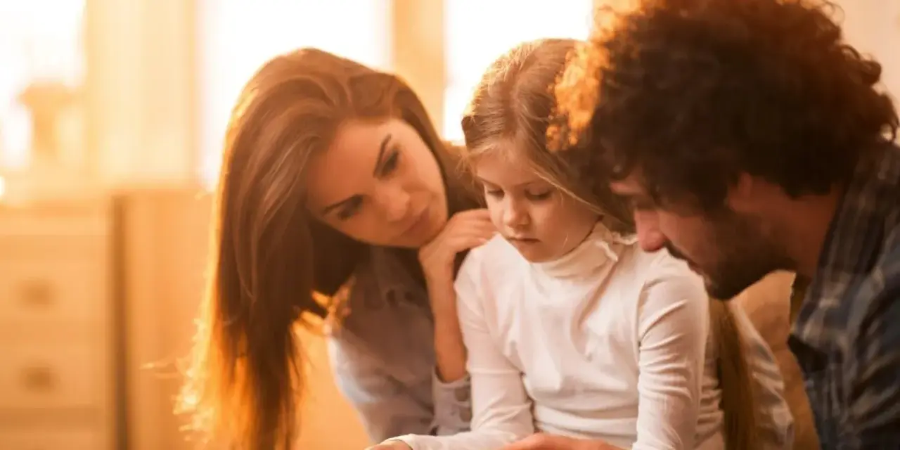 Eltern psychisch kranker Kinder spenden Trost. Ein Vater hält die Hände seiner Tochter, während die Mutter sie zärtlich berührt.