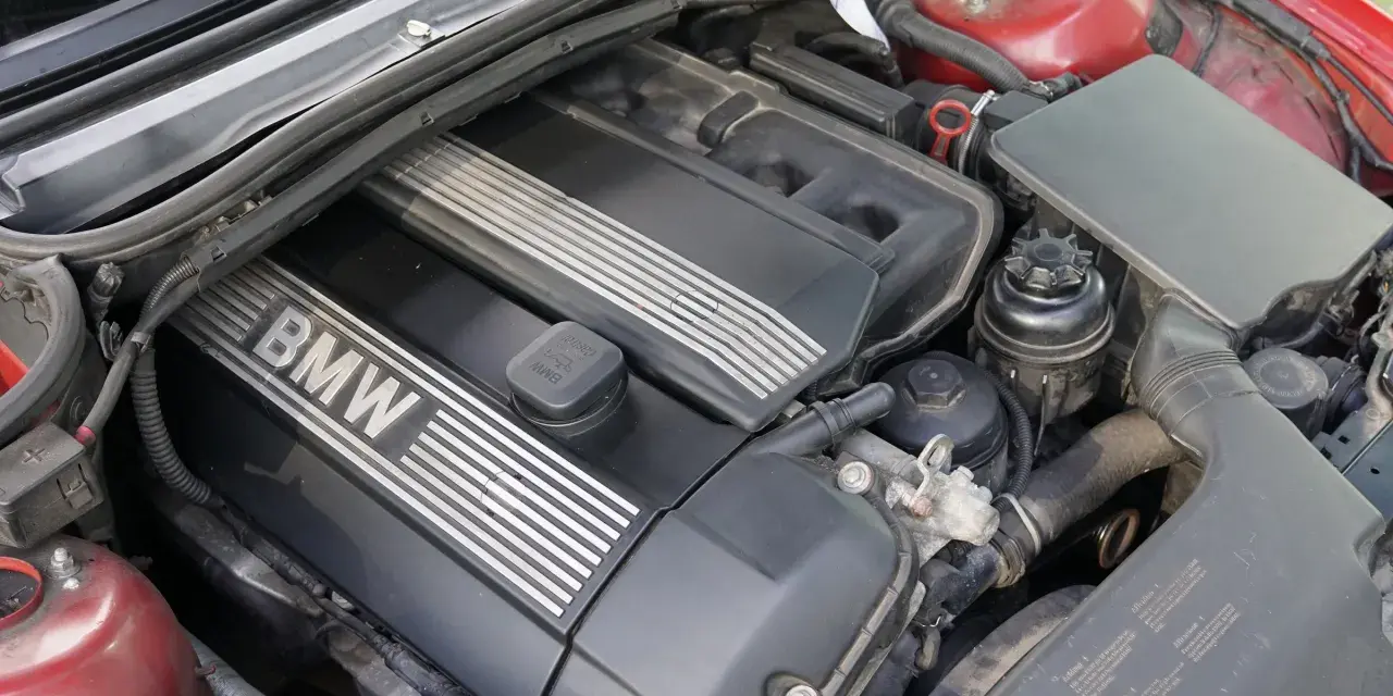 Silniki BMW E46, widok z góry na czarną pokrywę z napisem BMW i srebrnymi paskami. Widać też elementy układu dolotowego i zbiorniczek płynu.