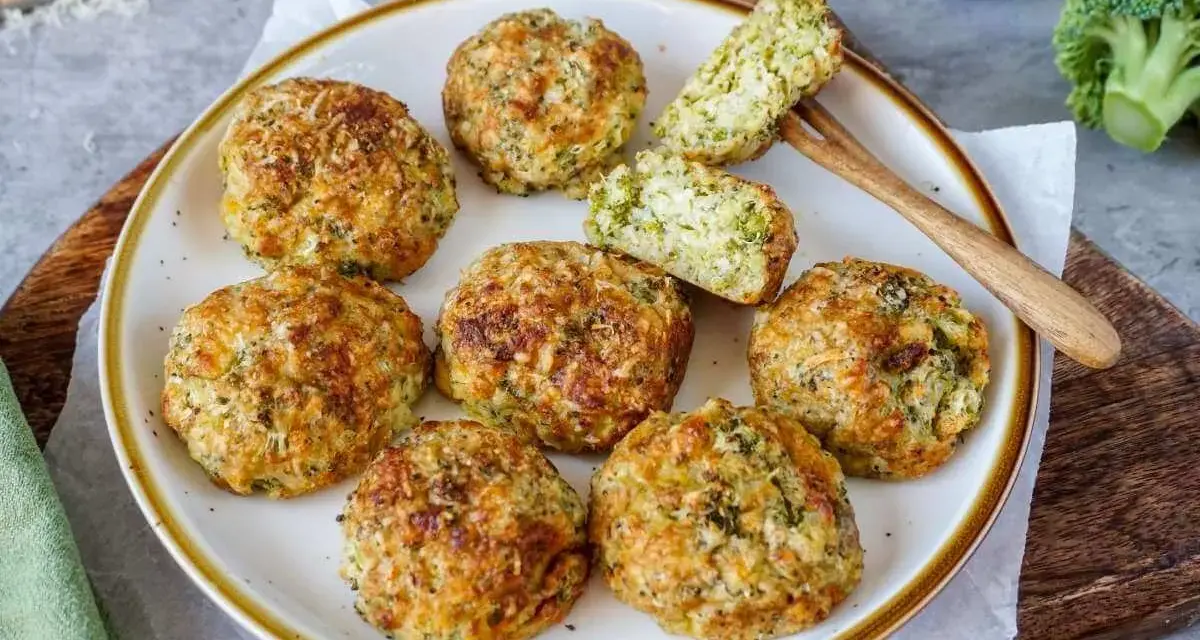Goldbraune, knusprige broccoli nuggets auf einem Teller, ein Stück angeschnitten, mit frischem Brokkoli im Hintergrund.