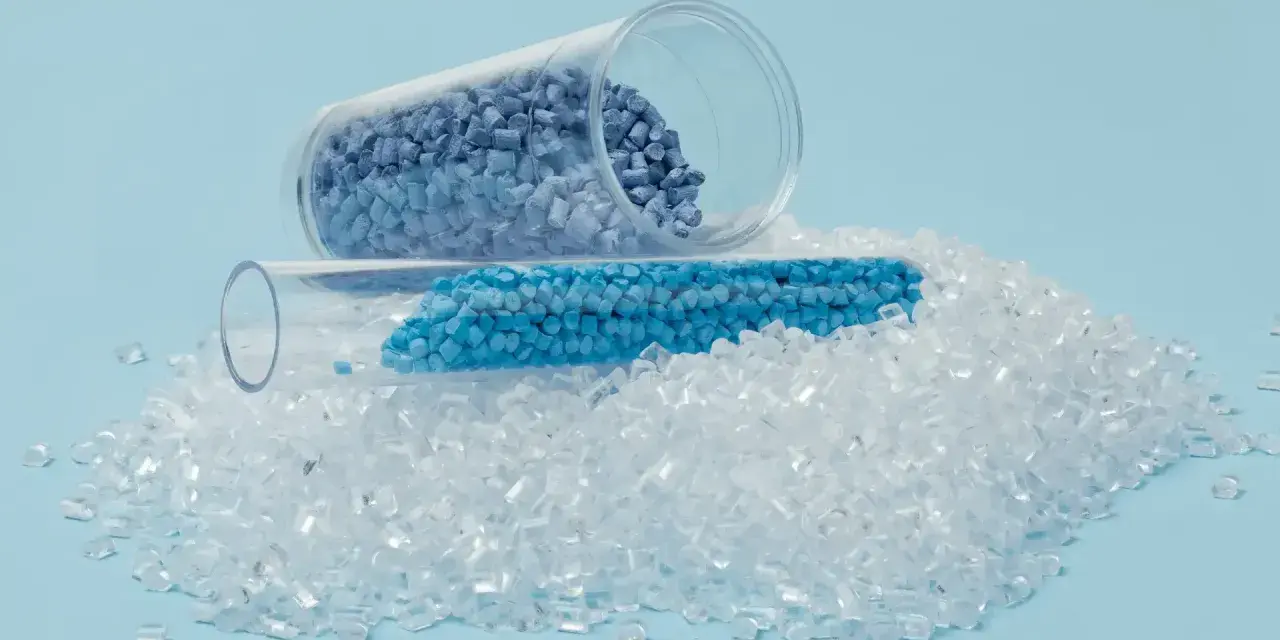 Granulat plastiku w probówkach i rozsypany na jasnoniebieskim tle.