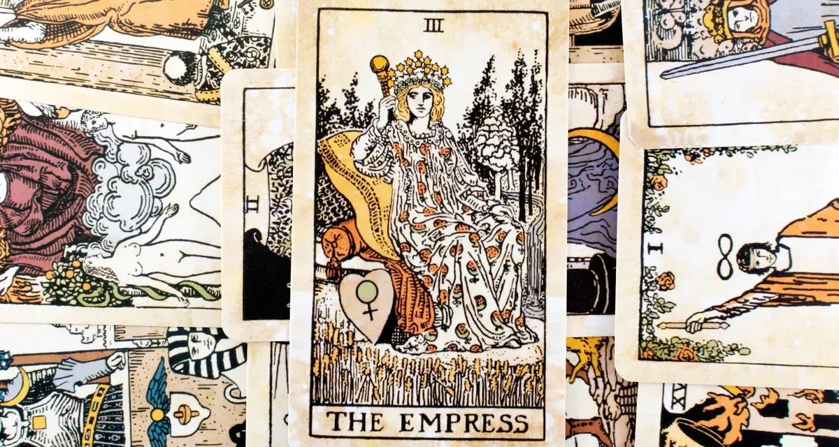 Karta Tarota "The Empress" w otoczeniu innych kart. Królowa siedzi na tronie, trzymając berło, symbolizując płodność i obfitość.