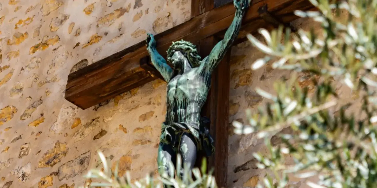 Brązowy Jezus na krzyżu, symbol chrześcijaństwa, na tle kamiennej ściany.