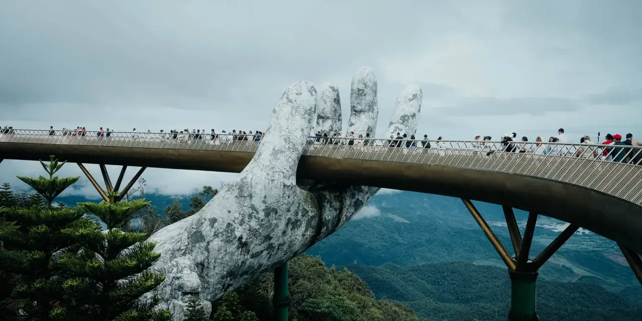 Goldene Brücke in Vietnam, gehalten von einer riesigen Steinhands. Touristen spazieren über die Brücke, die sich durch üppige grüne Berge schlängelt.