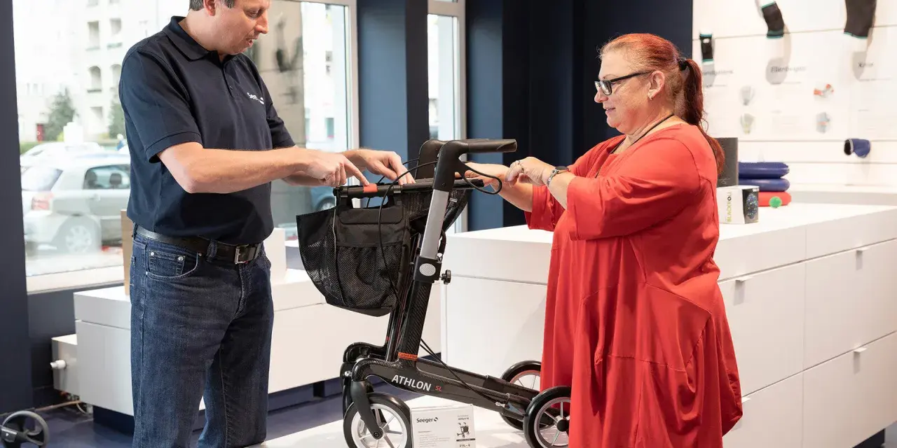 Mann erklärt einer Frau einen Rollator, ein wichtiges medizinisches Hilfsmittel, im Sanitätshaus.