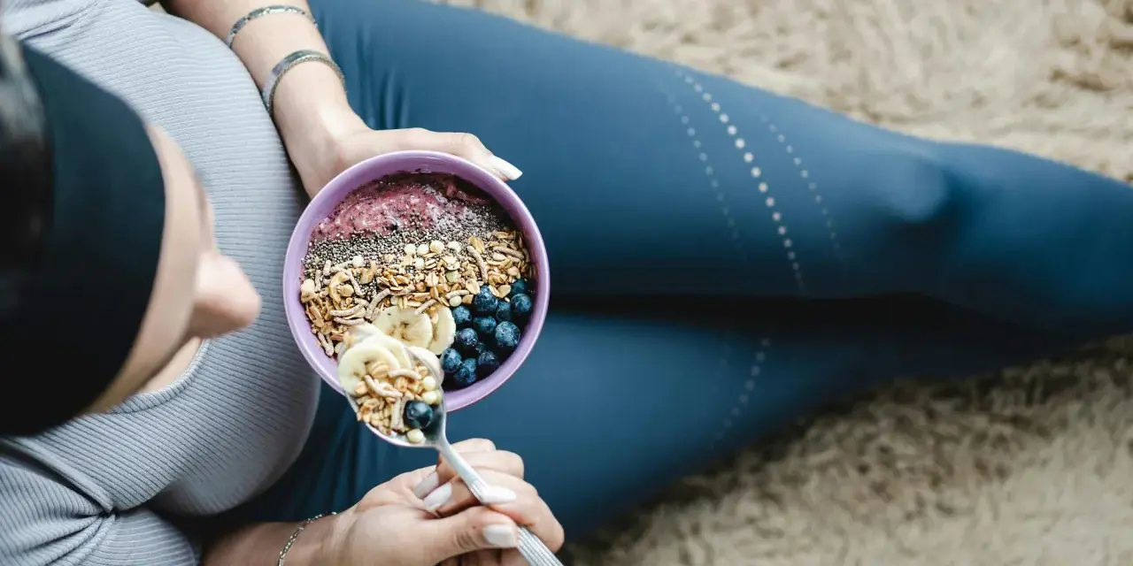 En kvinna äter en näringsrik skål med granola, bär och banan. En bra frukost kan bidra till att uppnå rekommenderat intag av hur mycket protein per dag kvinna.