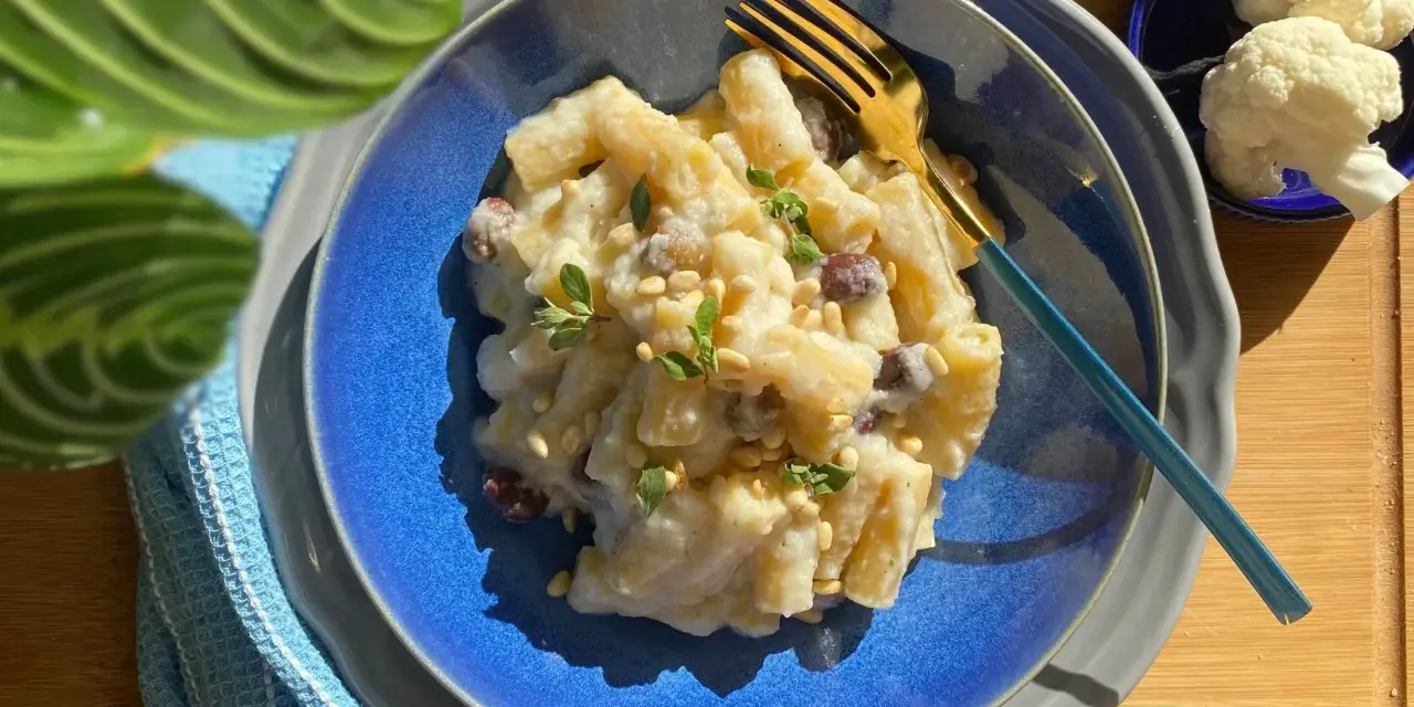 Piatto di pasta con cavolfiore cremoso, guarnito con pinoli e erbe aromatiche. Un primo piatto gustoso e leggero.