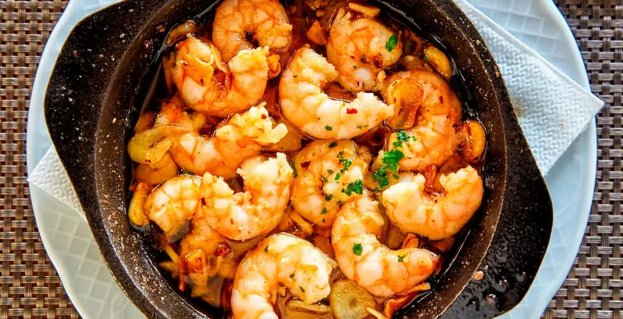 Un plato humeante de langostinos al ajillo, jugosos y dorados, nadando en aceite de oliva con ajo y perejil. ¡Un manjar irresistible!