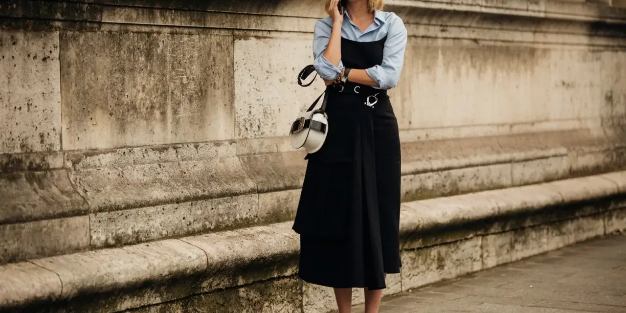 Mujer con un elegante vestido negro sobre una camisa blanca, hablando por teléfono.