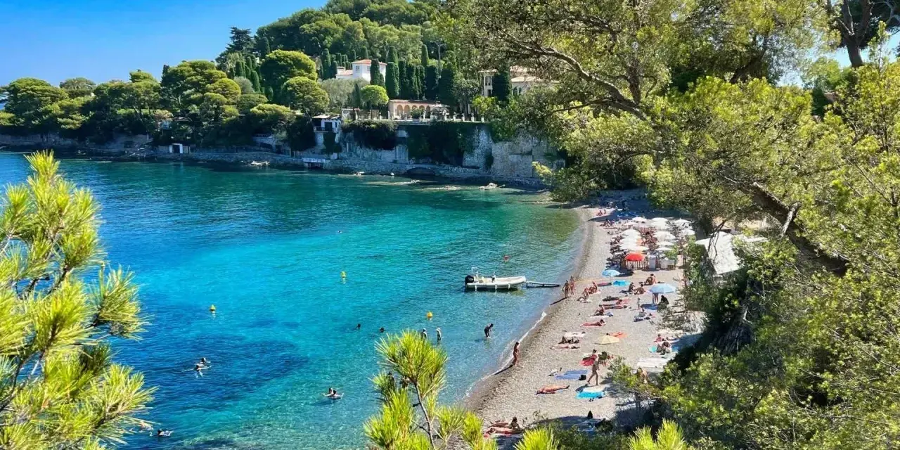 Plage idyllique à Antibes, eaux turquoise, pins parasols et villas sur la falaise. Parfait pour visiter Antibes et se détendre.