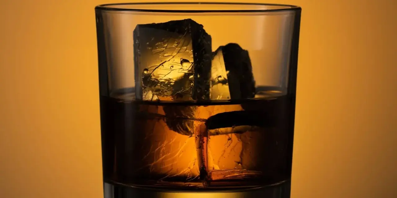 Ein Glas mit **whiskey neat**, zwei große Eiswürfel darin, beleuchtet von warmem Licht.