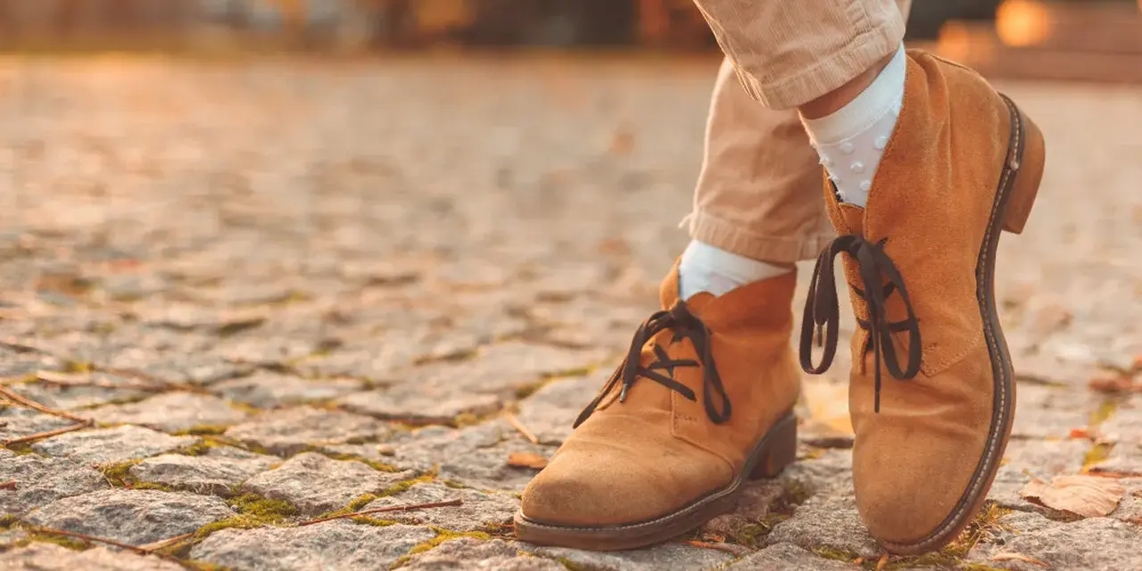 Herbstliche Stiefeletten aus Nubukleder, was das ist, zeigen sich auf einem Kopfsteinpflaster.