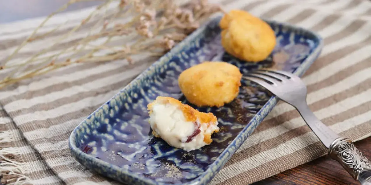 Croquetas de jamón doradas y cremosas en plato azul, una partida.