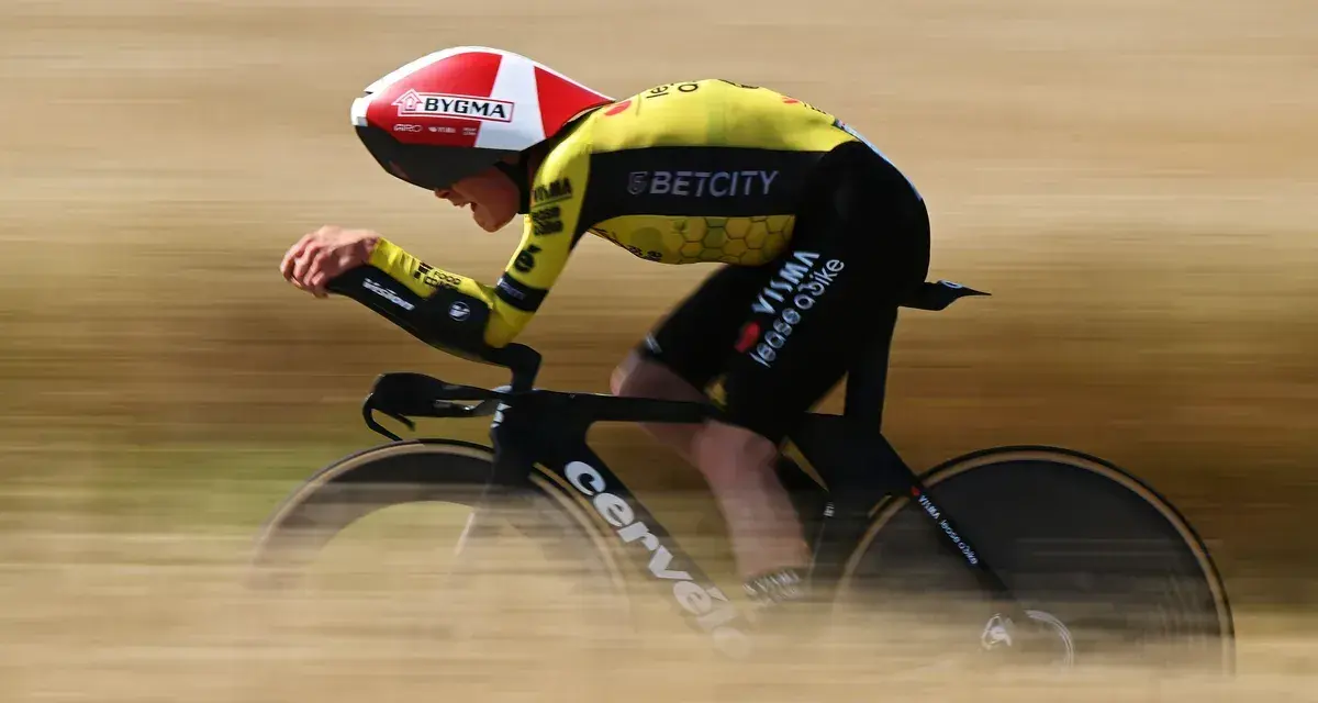A cyclist in a yellow and black suit, helmet, and aero bars races during the Dauphine cycling event, blurring past the camera.