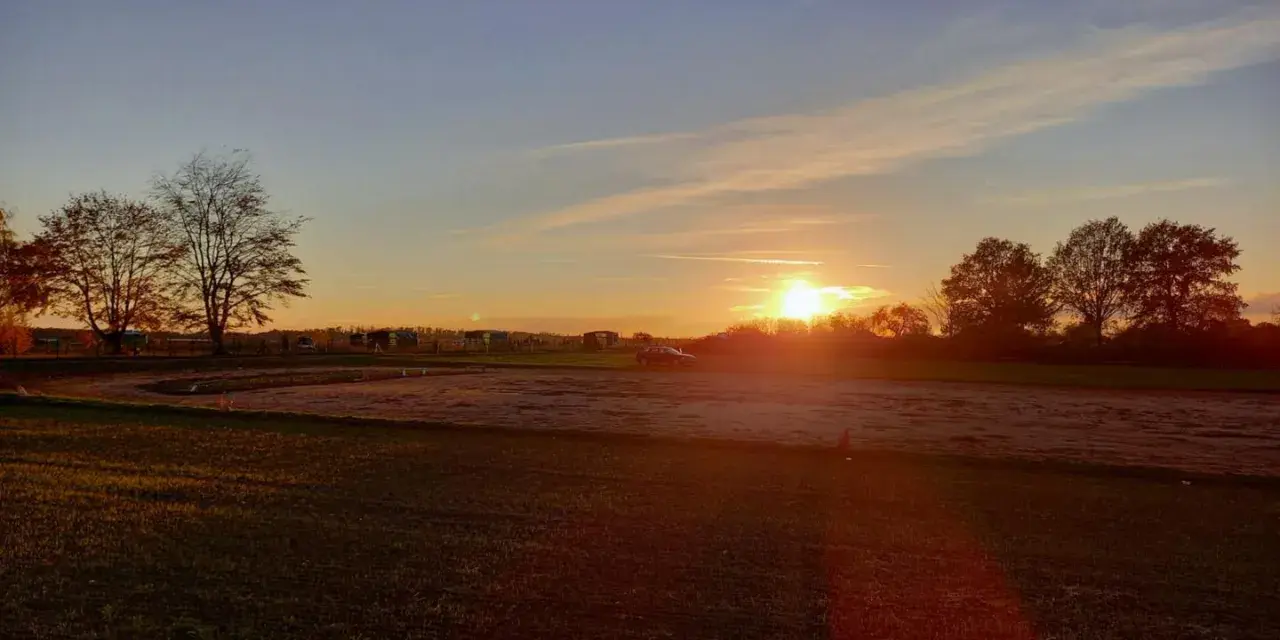 Sonnenuntergang über einem Feld mit Bäumen und einem Auto. "Seid stille und wisset: Ich bin Gott." (Psalm 46:10)
