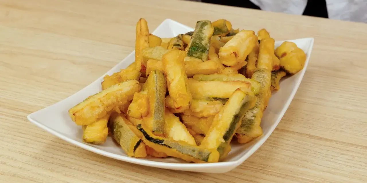 Un piatto bianco pieno di zucchine in pastella dorate e croccanti, pronte per essere gustate.