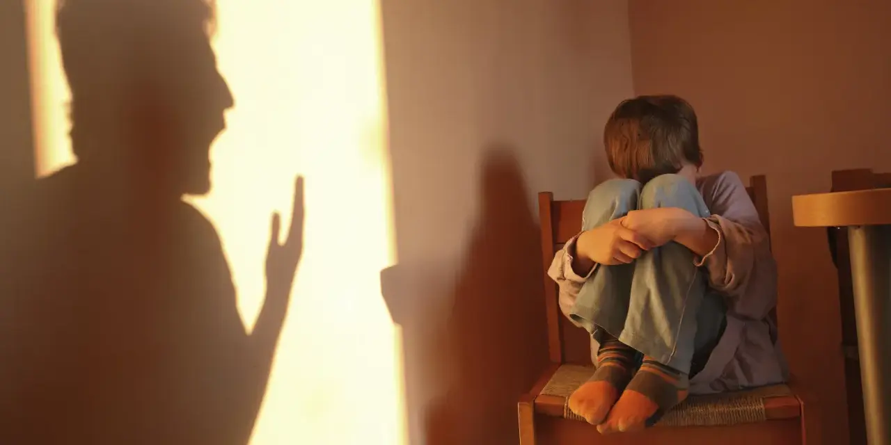 Cień krzyczącego dorosłego rzuca się na ścianę, podczas gdy dziecko skulone na krześle czeka na bicie po pupie.