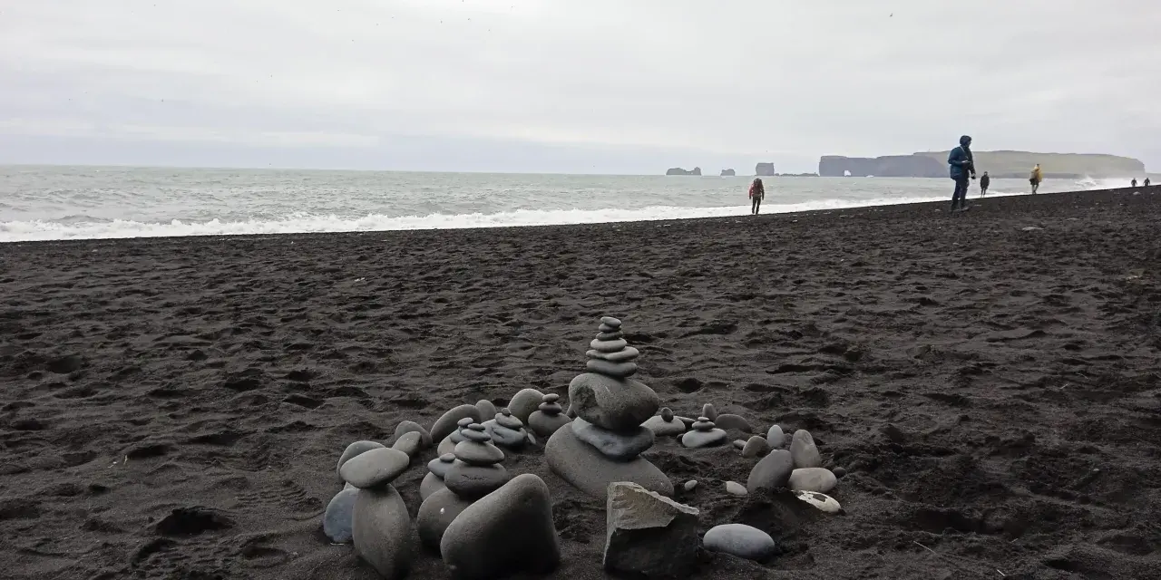 Kamienne stosy na czarnej plaży Islandii, z widokiem na ocean i skaliste wybrzeże.