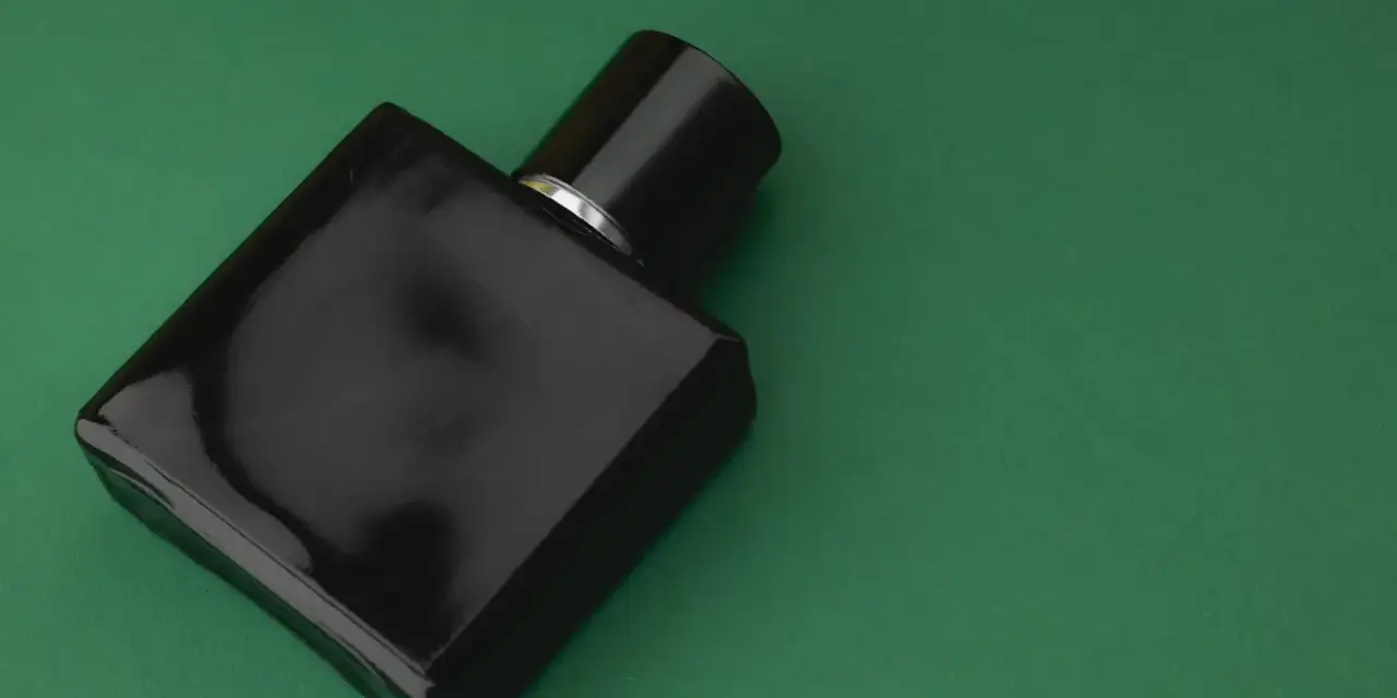 Czarna, elegancka butelka perfum z nutą wetiwery na zielonym tle.