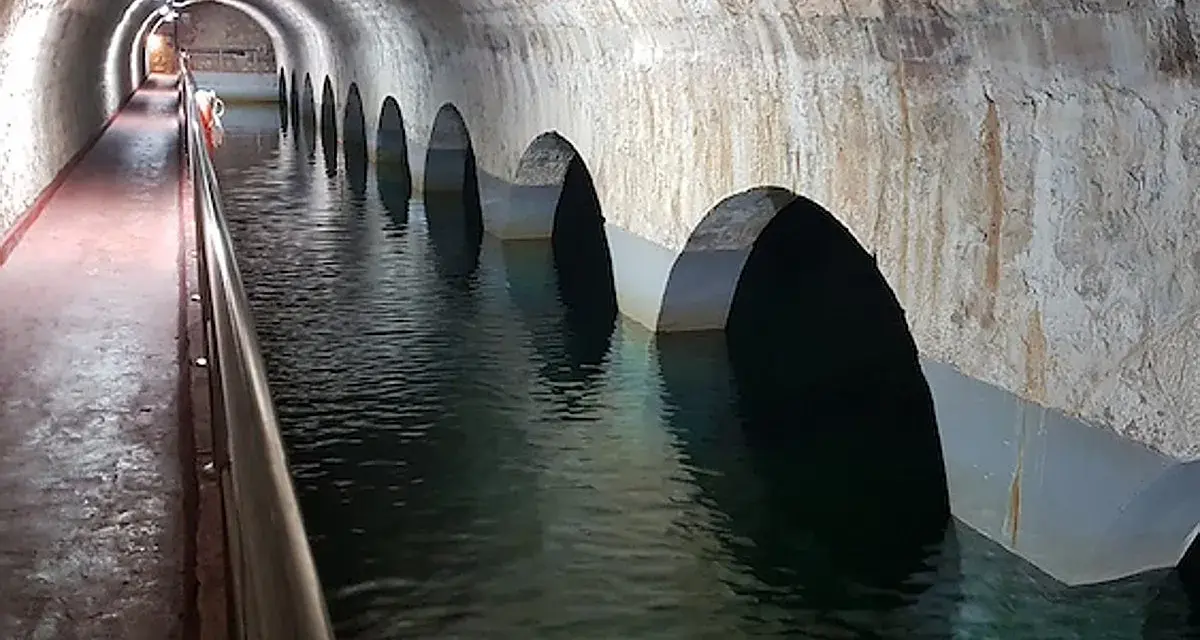 Interior de aljibes de agua abovedados, con arcos que se sumergen en el agua. Un pasillo con barandilla recorre el lateral.