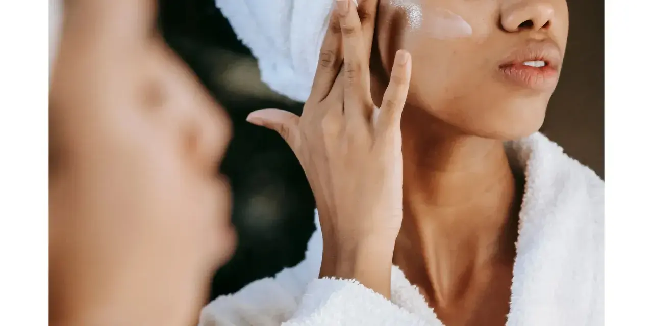Une femme applique une crème hydratante sur sa joue, un geste essentiel pour savoir comment bien hydrater son visage et obtenir une peau éclatante.
