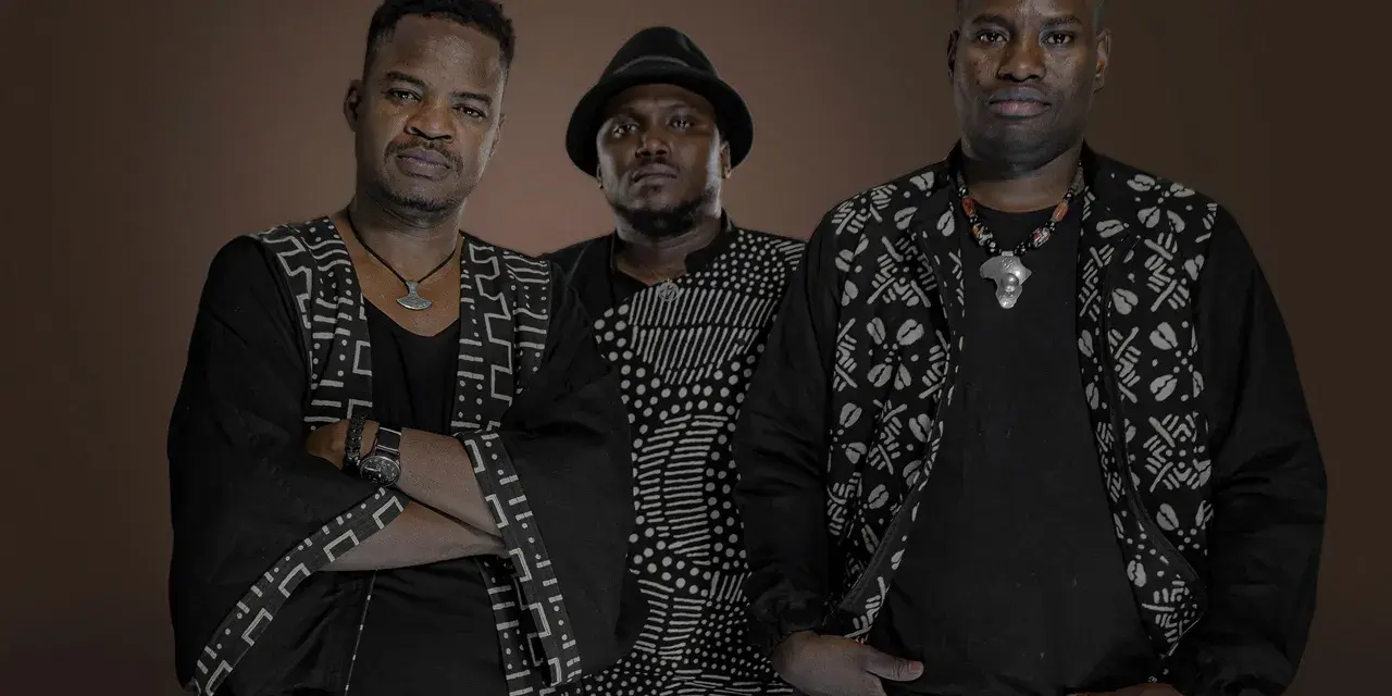 Trois hommes en tenue traditionnelle africaine, évoquant l'ancêtre du blues, posent avec assurance.