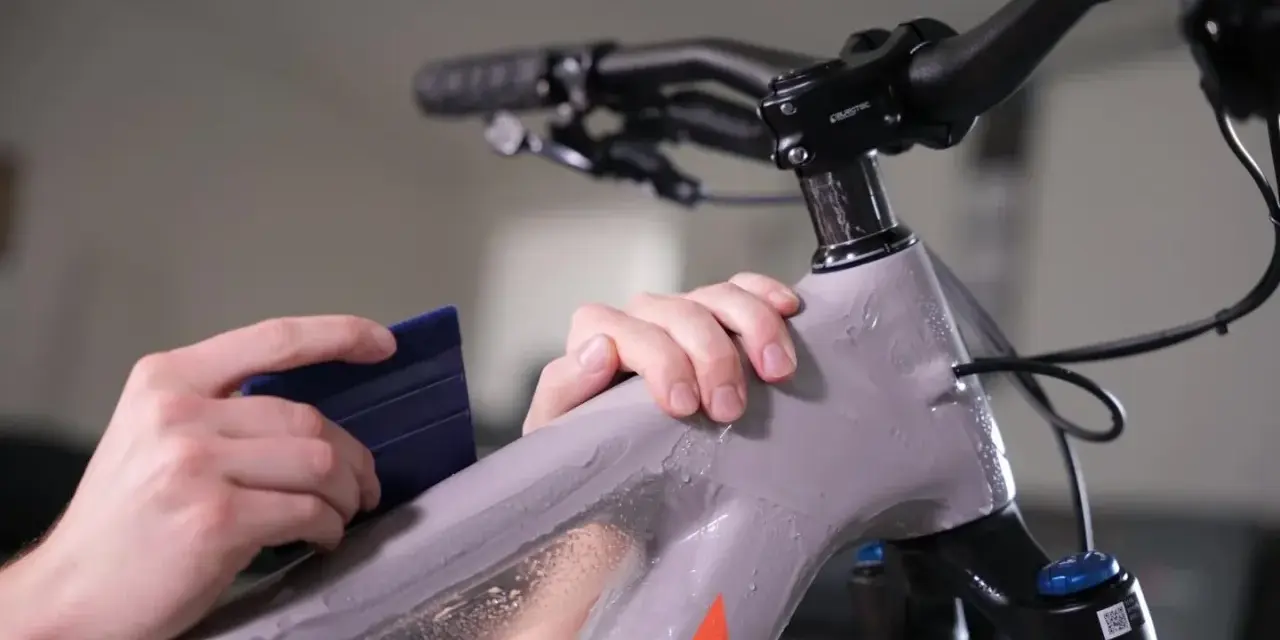 Hands apply protective film to a mountain bike frame. This bike is ready for any terrain, whether trails or roads.