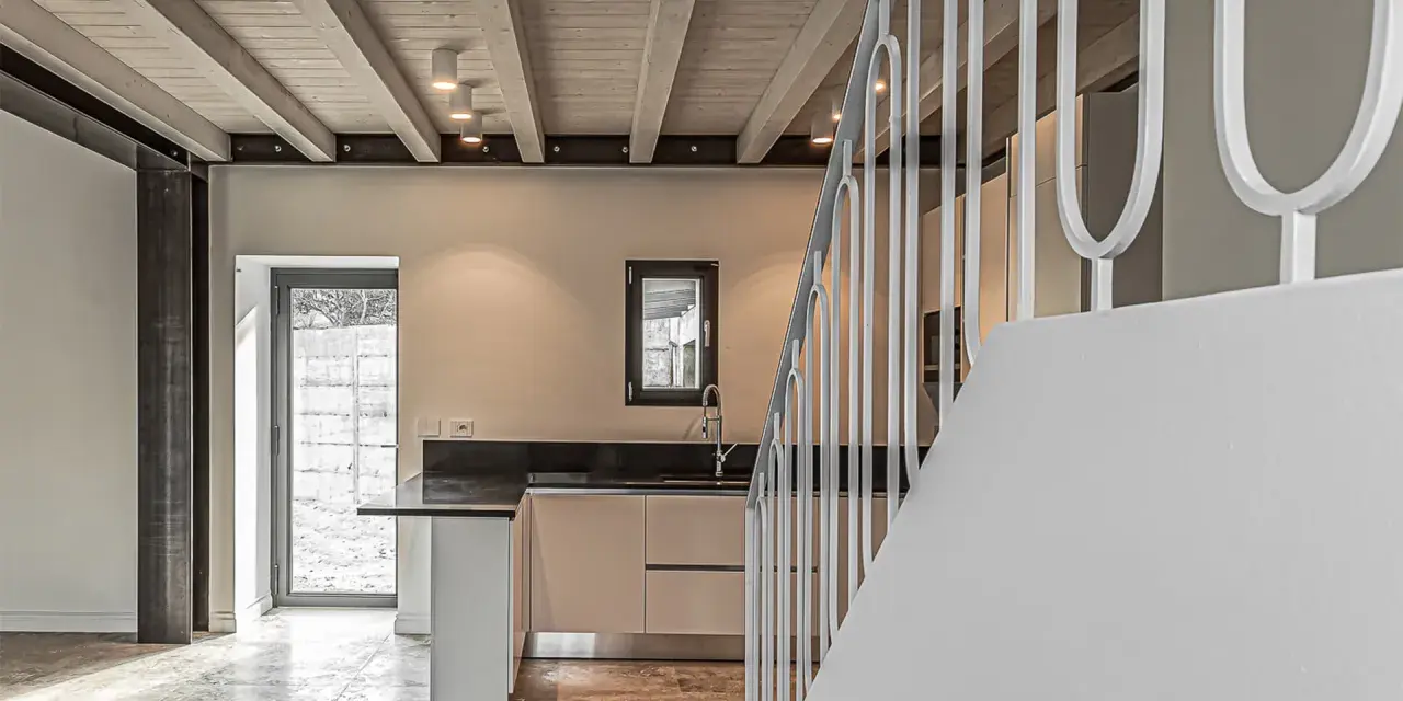 Interno moderno con travi a vista in legno, illuminazione led soffusa e una scala bianca.